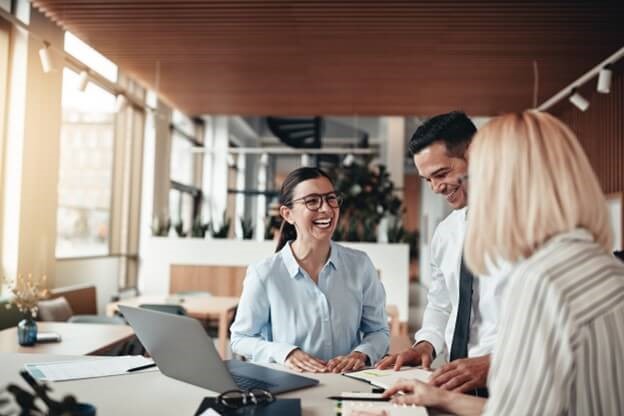 three employees laughing around a laptop