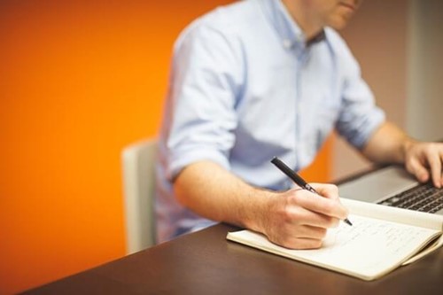 Someone making notes while using a laptop